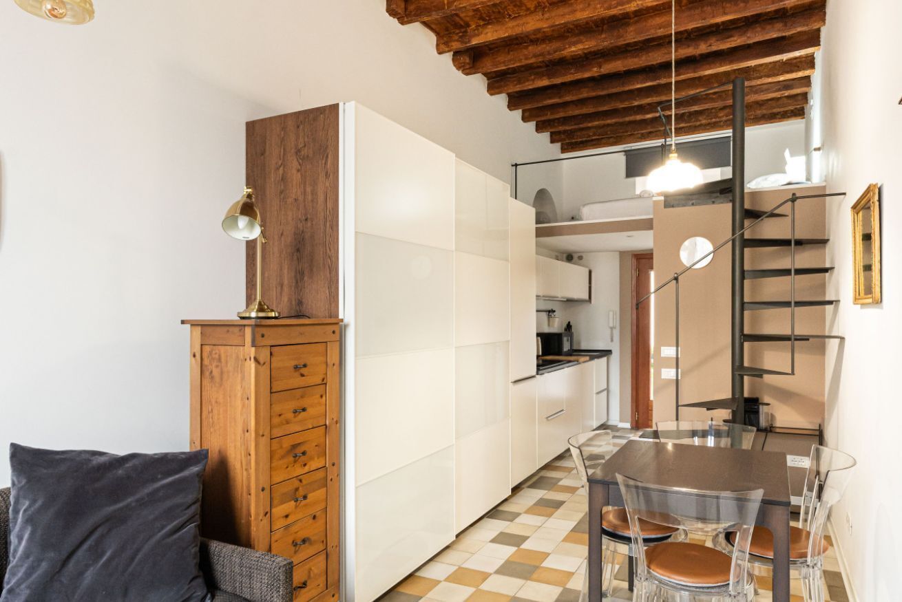 A compact kitchen with white cabinets, a wooden cabinet, and a dining area with a table and chairs.