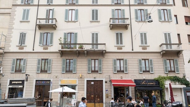 A multi-story building with a row of shops on the ground floor, including a café and a clothing store. - One bedroom Corso Garibaldi - Mirable PM (Milano)