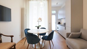 A modern living space with a dining area, a sofa, a TV, and a kitchen in the background. - One bedroom San'Agostino - Mirable PM (Milano)