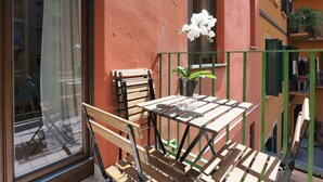 A balcony with a wooden table and chairs, a potted plant, and a window with a view of buildings. - One bedroom San'Agostino - Mirable PM (Milano)