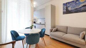 A modern living room with a round dining table, blue chairs, a beige sofa, and a painting of a night sky. - One bedroom San'Agostino - Mirable PM (Milano)