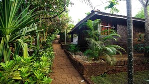 A pathway leading to a rustic building surrounded by lush greenery and tropical plants. - Namaste Yoga Farm (Kumta)