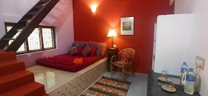 A bedroom with a bed, a chair, a lamp, a picture on the wall, and a staircase. - Namaste Yoga Farm (Kumta)