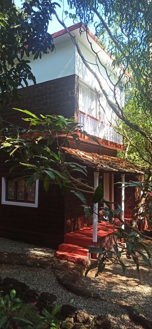 A two-story building with a red roof, white columns, and a small porch with steps. - Namaste Yoga Farm (Kumta)