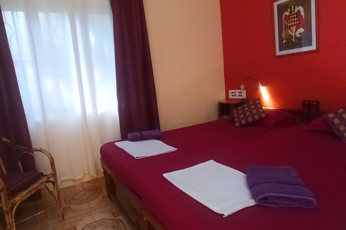 Een hotelkamer met een bed, een stoel, een nachtkastje, een lamp en een poster aan de muur.