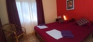 Een hotelkamer met een bed, een stoel, een nachtkastje, een lamp en een poster aan de muur.