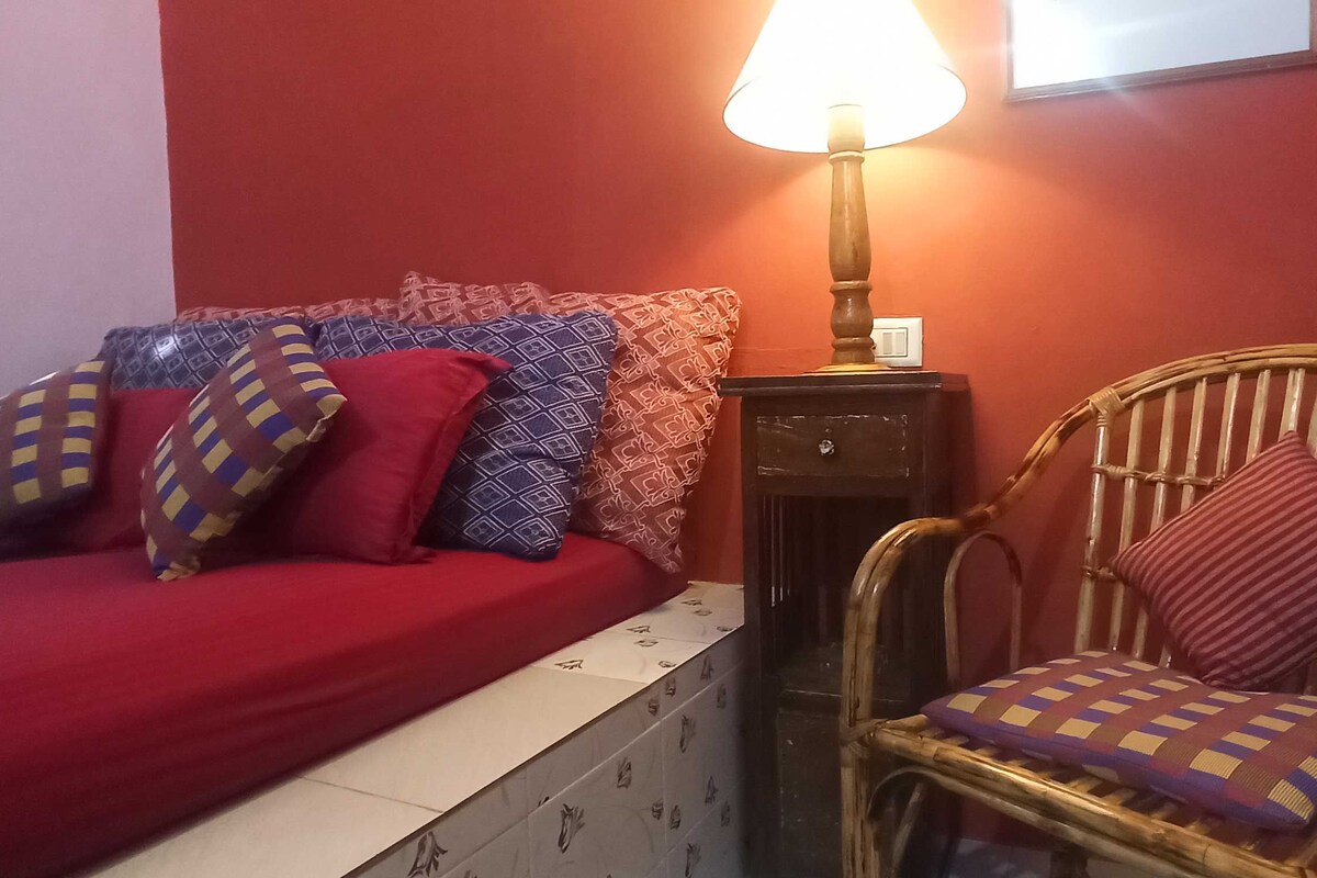 A room with a bed, a chair, a lamp, and a wall-mounted light switch.