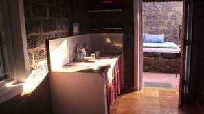 A kitchen with a stone wall, a window, and a door leading to a balcony. - Namaste Yoga Farm (Kumta)