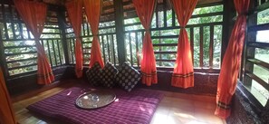A room with a wooden ceiling, a window with red curtains, a purple mat, and a woven tray. - Namaste Yoga Farm (Kumta)