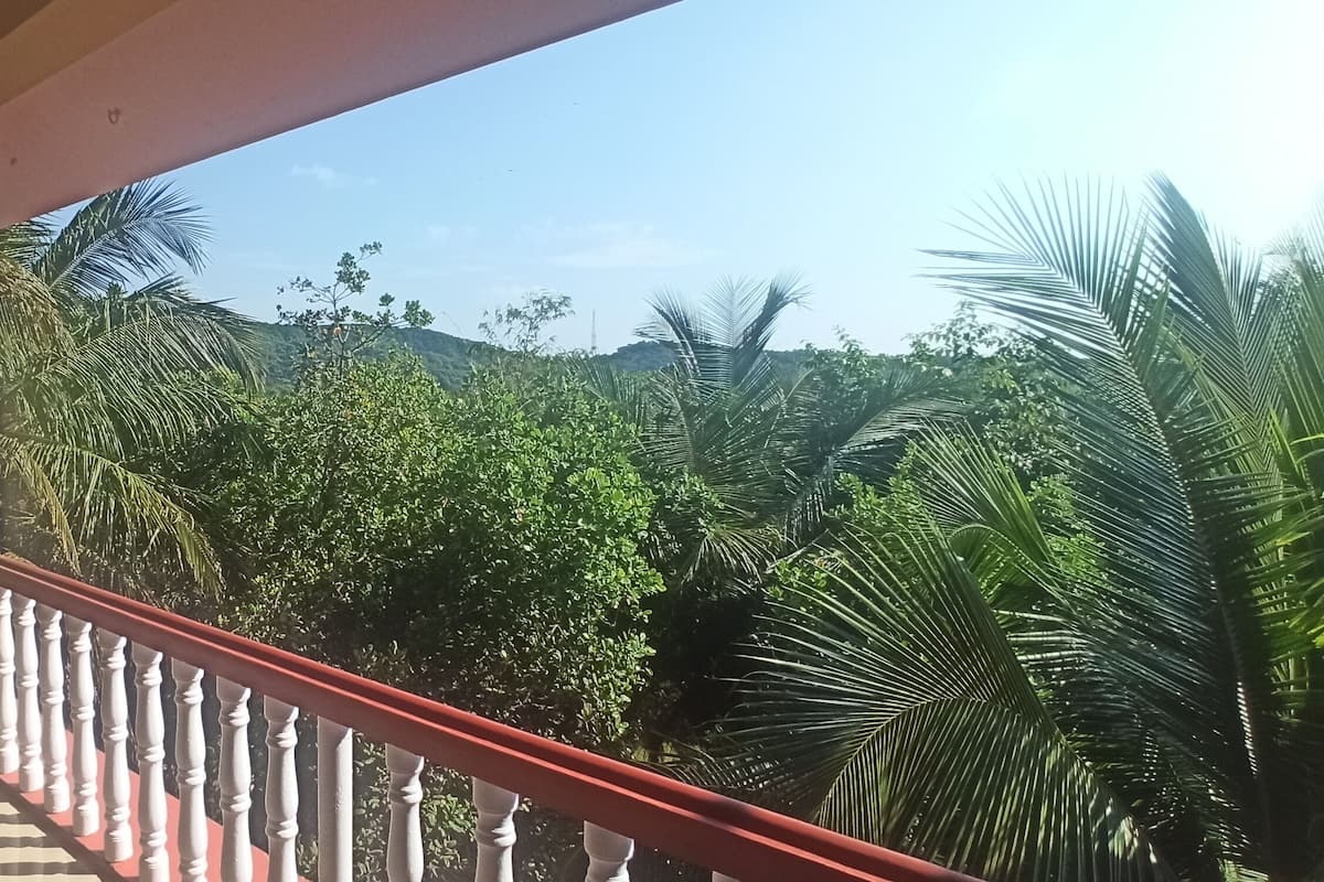 Un balcón con barandilla roja que da a un paisaje verde exuberante, con palmeras y colinas al fondo.