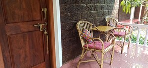 A wooden door with a brass handle, a stone wall, and two wicker chairs with colorful cushions. - Namaste Yoga Farm (Kumta)