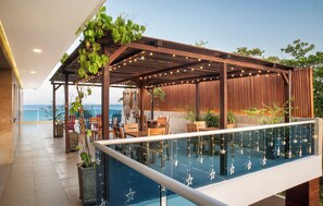 Un espace extérieur abrité, aménagé avec des tables et des chaises, offrant une vue sur une piscine et la mer.