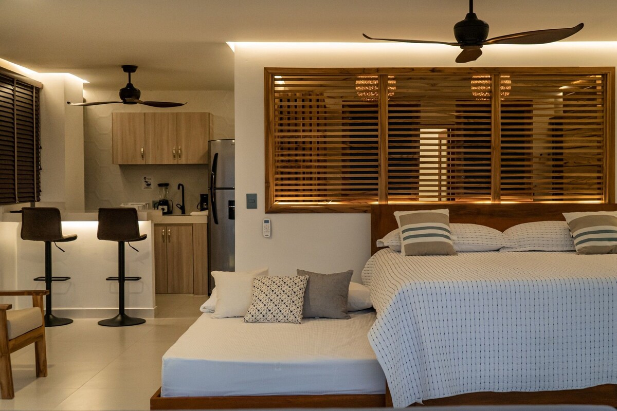 Een slaapkamer met een bed, nachtkastjes, een bureau en een kitchenette.