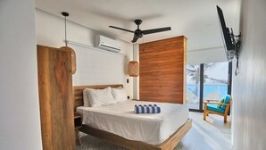 A bedroom with a wooden bed, white bedding, a ceiling fan, and a view of the ocean.