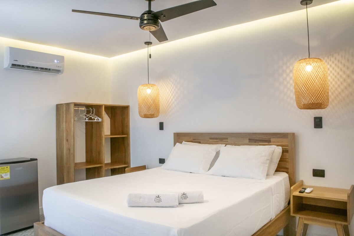 Hotelkamer met een bed, houten hoofdeinde, twee hanglampen, een garderobe, nachtkastje en een airconditioning.