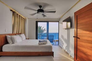 Een slaapkamer met een bed, een plafondventilator, een aan de muur bevestigde televisie en een balkon met uitzicht op zee.