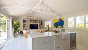 A modern living room with a large white sofa, a flat-screen TV, and a bookshelf. - The Island Veranda - Our Island (Waiheke Island)