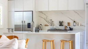 A modern kitchen with white cabinetry, a marble backsplash, and a central island with stools. - The Island Veranda - Our Island (Waiheke Island)