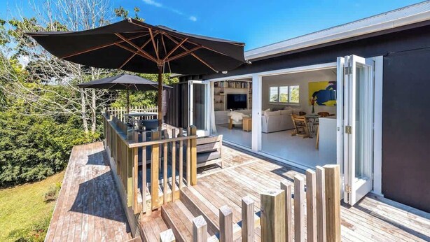 A modern house with a deck, outdoor seating, and a large umbrella. - The Island Veranda - Our Island (Waiheke Island)