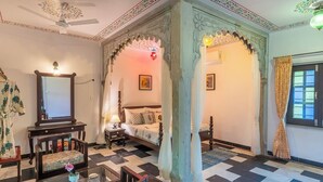 Una habitación tradicional con cama, zona de estar con mesa y sillas, y un arco decorativo.