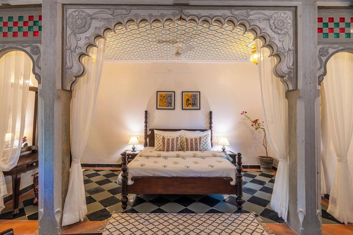 A room with a checkered floor, a wooden bed with a canopy, two wall-mounted lamps, and a potted plant.