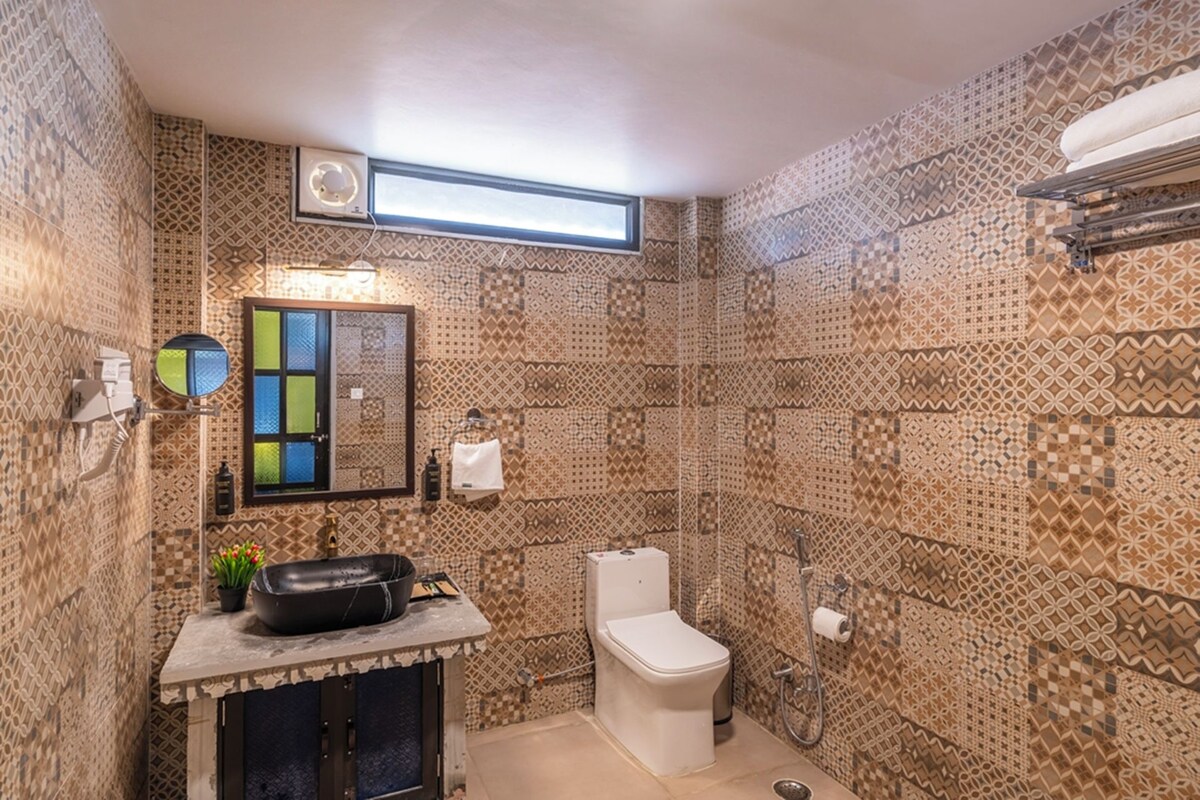 A bathroom with patterned walls, a sink with a mirror, a toilet, and a shower area.