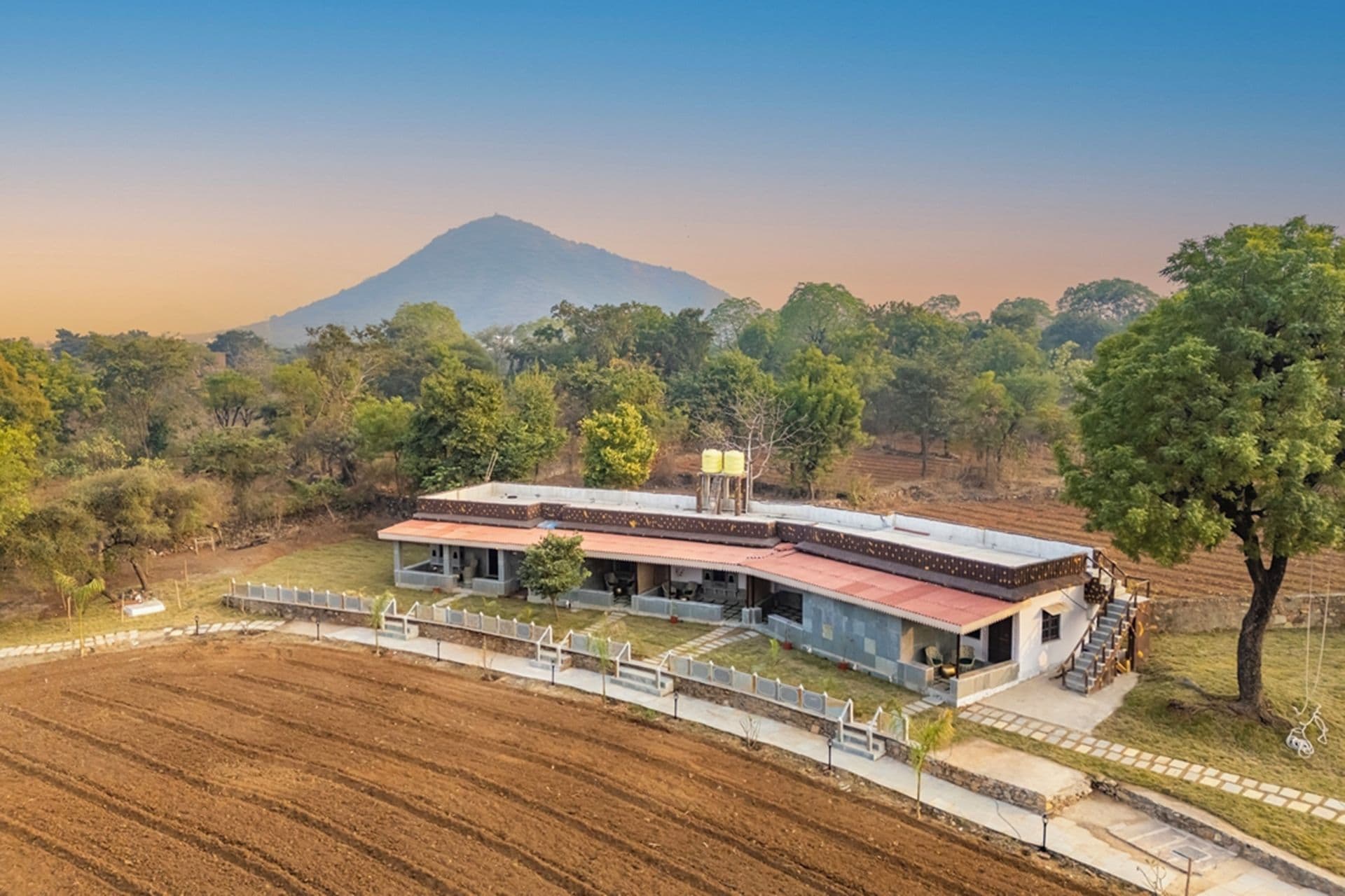 A modern house with a curved roof, surrounded by a fenced property, and a mountain in the background.