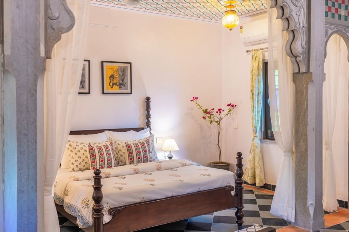 A traditional room with a bed, a nightstand, a lamp, and a vase with flowers.