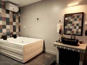 A modern bathroom with a large bathtub, a sink with a black basin, a towel rack, and a decorative mirror. - Indulge Udaipur By Pack (Udaipur)