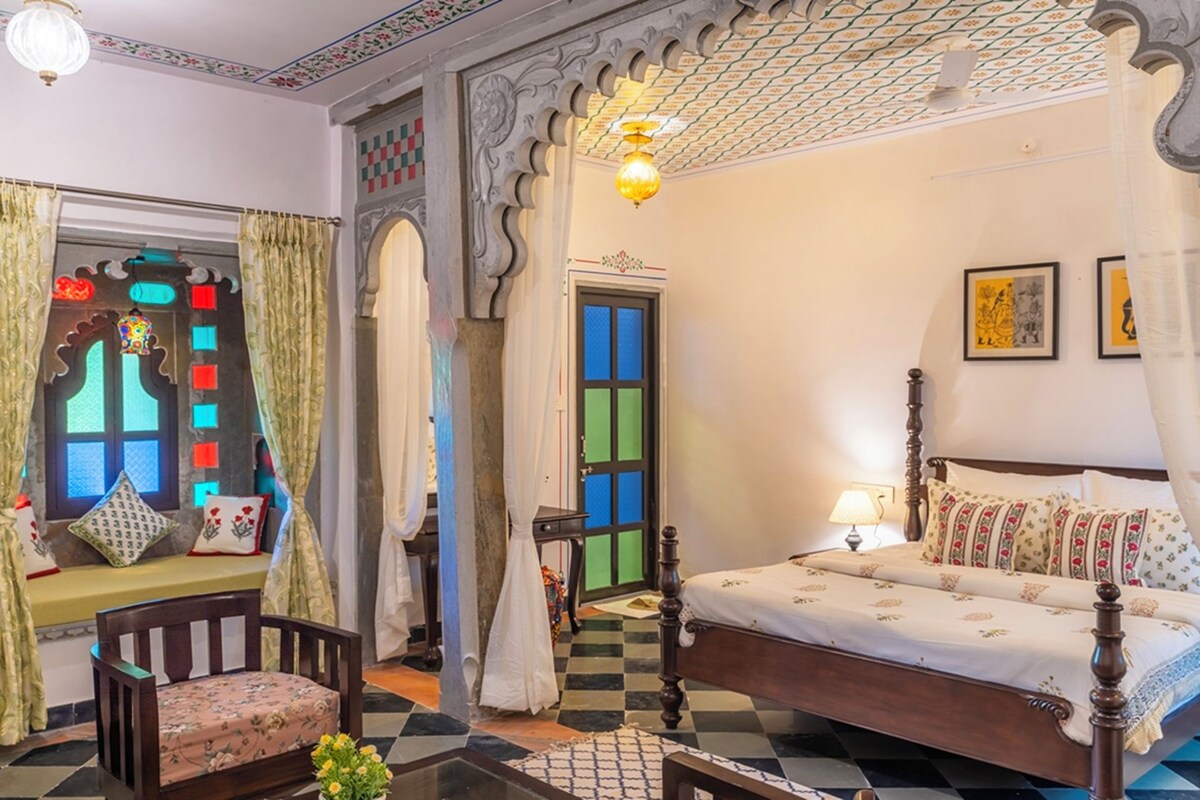 A traditional room with a bed, a chair, and a window with decorative curtains.