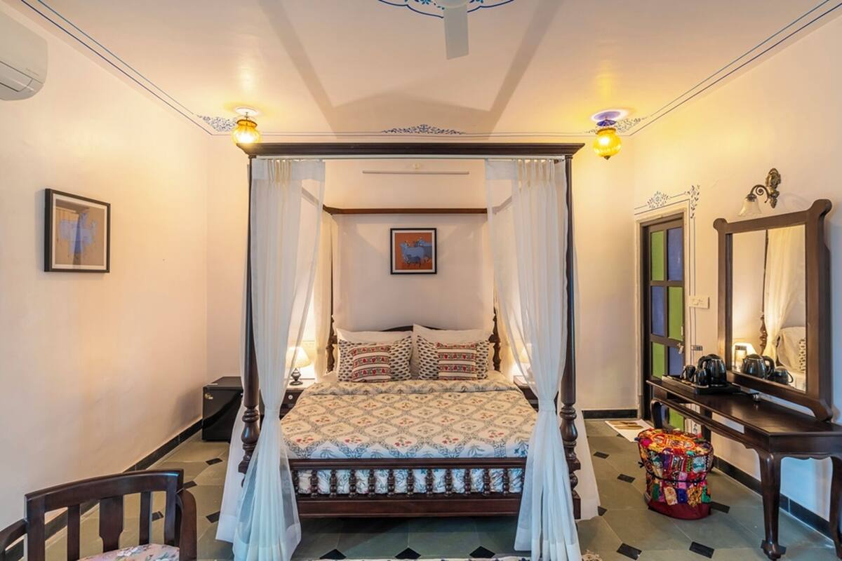 A four-poster canopy bed with a patterned bedspread, a bedside table with a lamp, and a mirror on the wall.