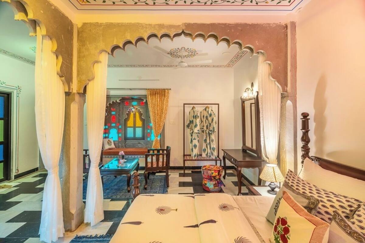 A traditional room with a bed, a small table, a chair, and a decorative mirror.
