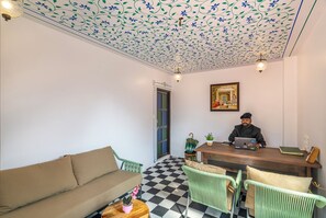 A room with a checkered floor, a sofa, a wooden desk, and a person working on a laptop. - Indulge Udaipur By Pack (Udaipur)