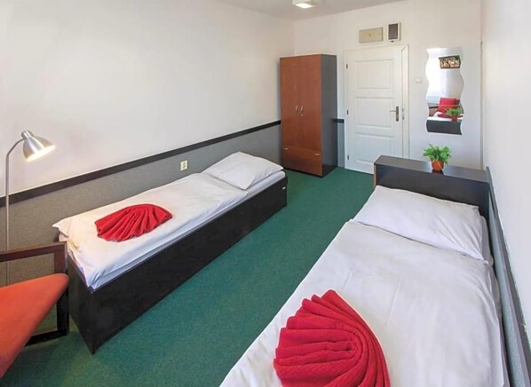 A hotel room with two single beds, a desk, a chair, a wardrobe, and a mirror. - Masarykova Kolej (Prague)