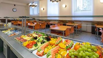 Una cafetería con una variedad de frutas y verduras exhibidas en un mostrador, rodeada de mesas y sillas.