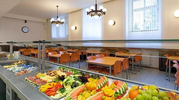 Una cafeteria amb una varietat de fruites i verdures exposades a un mostrador, envoltada de taules i cadires.
