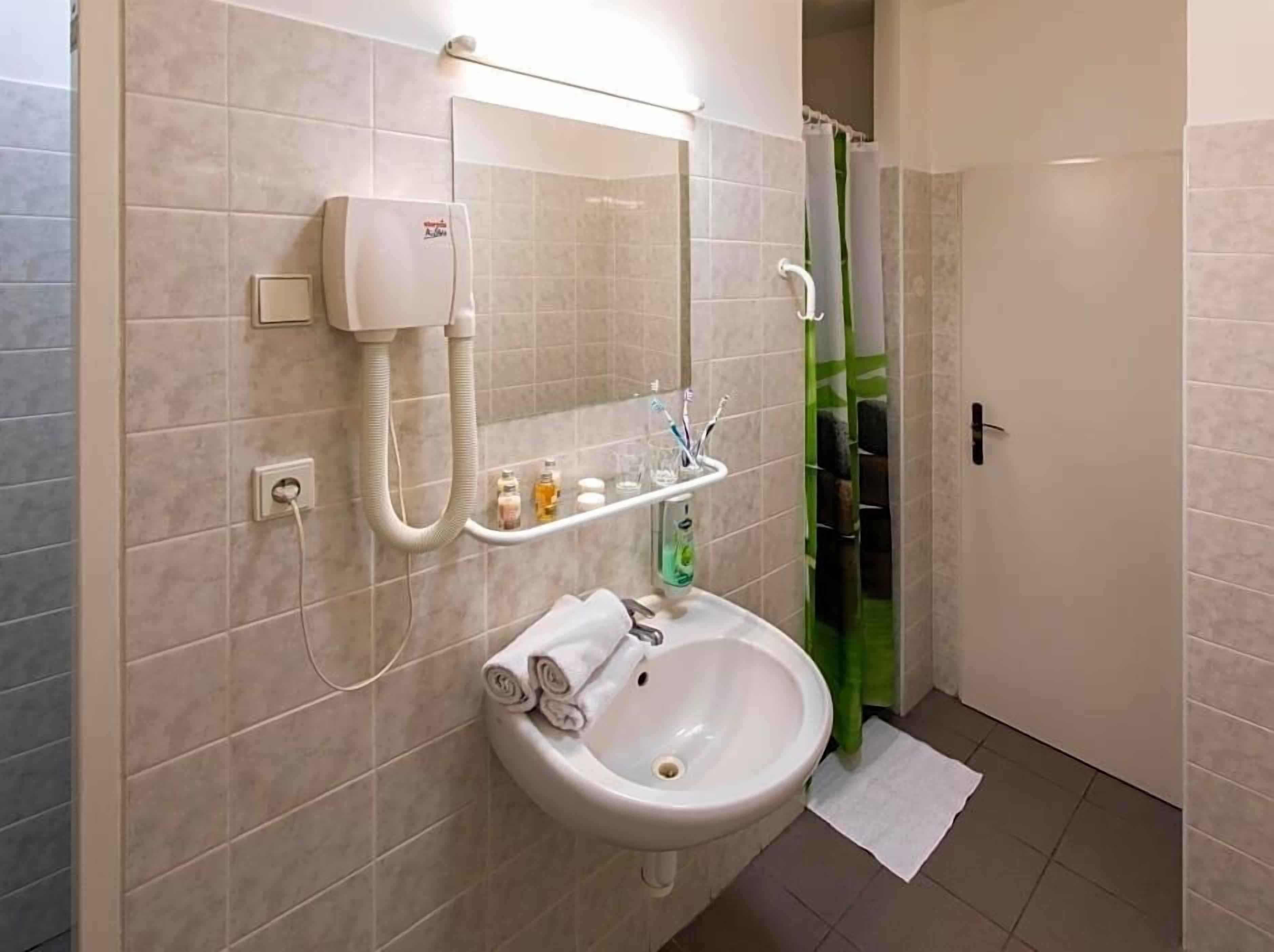 Un baño con lavamanos blanco, espejo, secador de pelo y cortina de ducha.
