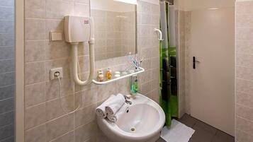 Un baño con lavamanos blanco, espejo, secador de pelo y cortina de ducha.