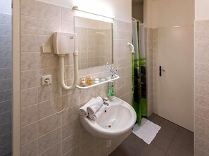 A bathroom with a white sink, a mirror, a hairdryer, and a shower curtain. - Masarykova Kolej (Prague)