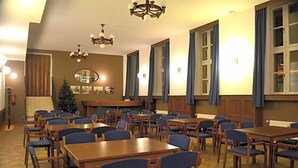 Una zona de menjador amb taules de fusta i cadires blaves, grans finestres amb cortines i un arbre de Nadal al fons.