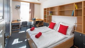 A hotel room with a large bed, a desk, a chair, and a wardrobe. - Masarykova Kolej (Prague)
