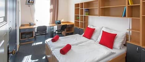 A hotel room with a large bed, a desk, a chair, and a wardrobe.