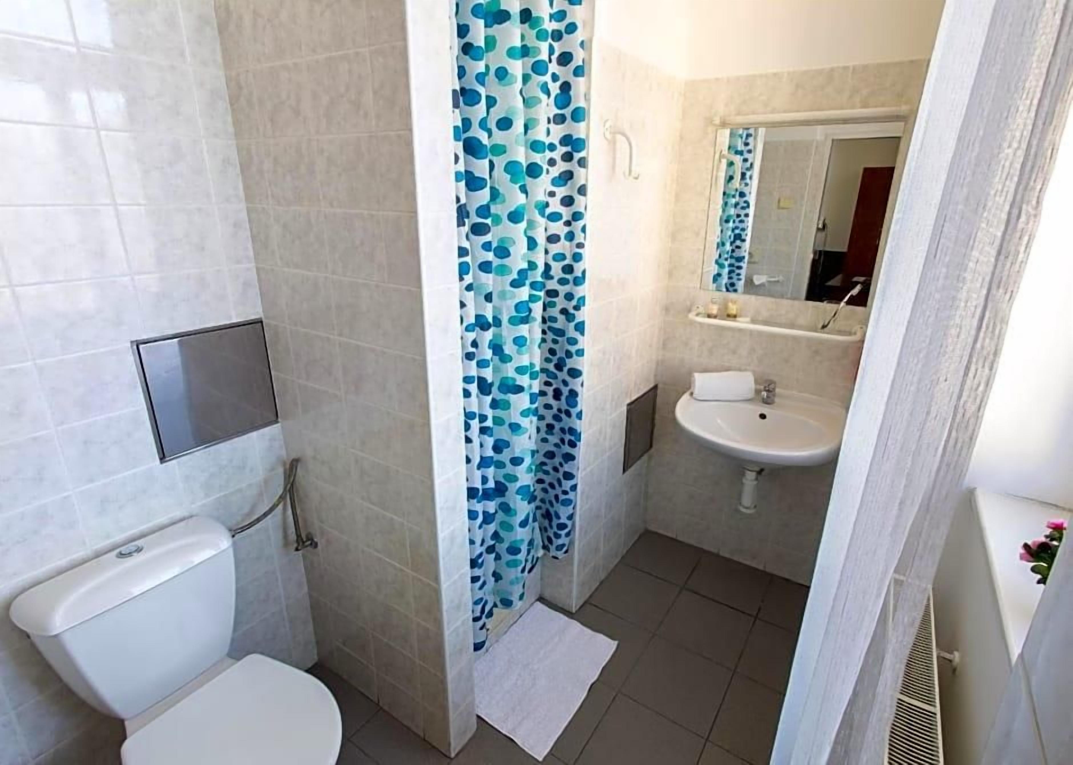 A bathroom with a toilet, a sink, a shower with blue polka dot curtains, and a mirror above the sink.