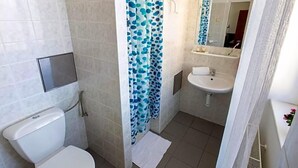 A bathroom with a toilet, a sink, a shower with blue polka dot curtains, and a mirror above the sink. - Masarykova Kolej (Prague)