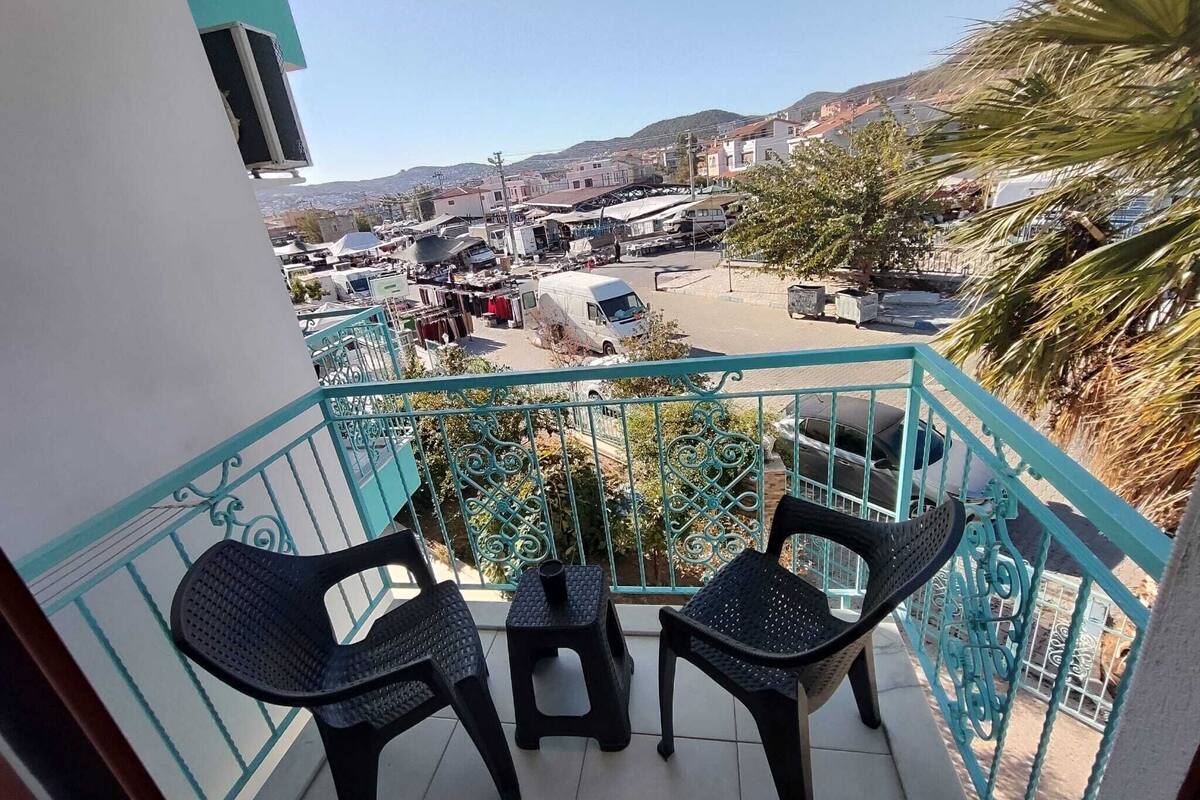 Un balcón con dos sillas y una mesa, con vista a un estacionamiento y edificios.