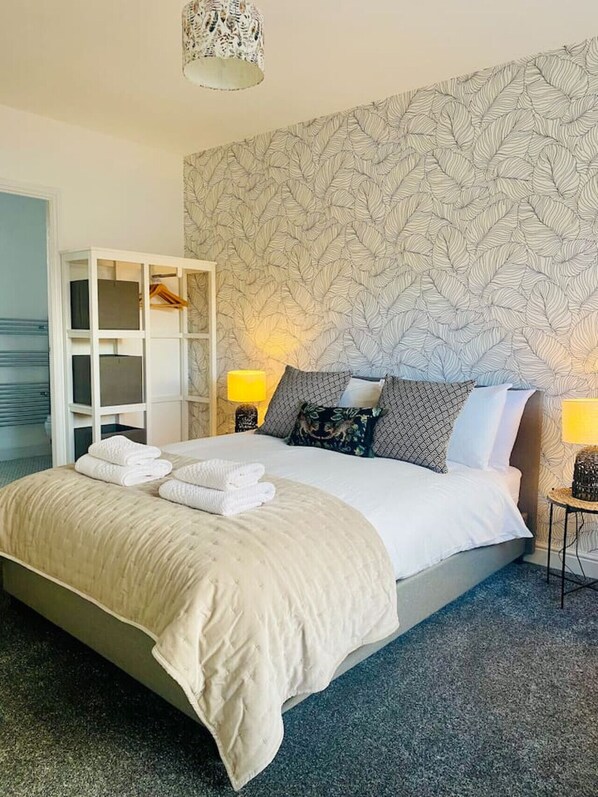 Un lit bien fait, avec une couette et des oreillers de couleur beige, une armoire blanche et un mur à motifs.