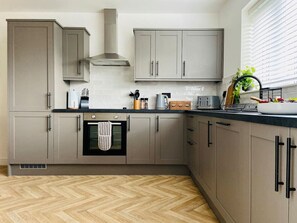 Una cocina moderna con armarios grises, suelo de madera en patrón de espiga y una ventana con persianas.
