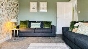 En stue med to mørkegrå sofaer, et rundt sofabord med en lampe, og tapet med mønster.