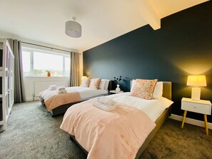 Ein Hotelzimmer mit zwei Betten, einem fensterbelaubten Fenster, einer Nachttischlampe und Blick ins Freie.