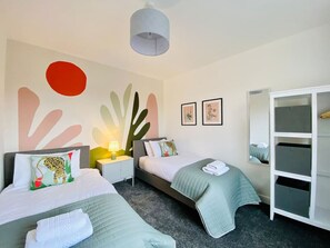 Een hotelkamer met twee bedden, een kledingkast, een nachtkastje met een lamp en abstracte wanddecoratie.